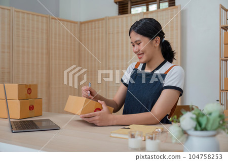 Woman runs an ecommerce business is writing a list of customers on box before shipping to customer, Concept of selling products online 104758253
