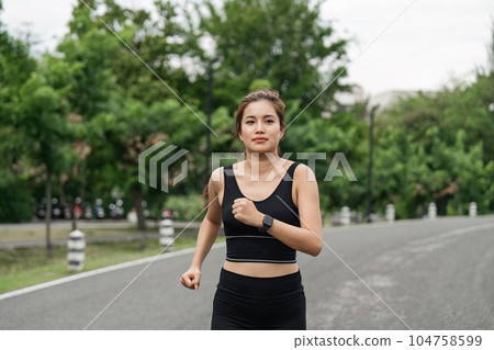 Young smiling sporty woman running in park in the morning. Fitness girl jogging in park 104758599