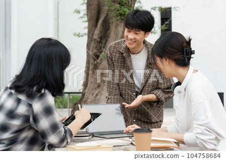 Group of happy students checking results on laptop and tablet while sitting on college campus, concept of education, technology and project work discussion 104758684