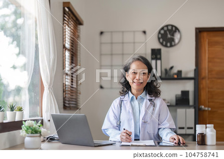 Portrait of smiling young Senior female doctor smiling sit at desk in hospital or private clinic, of happy positive female doctor in white medical uniform at workplace, healthcare 104758741