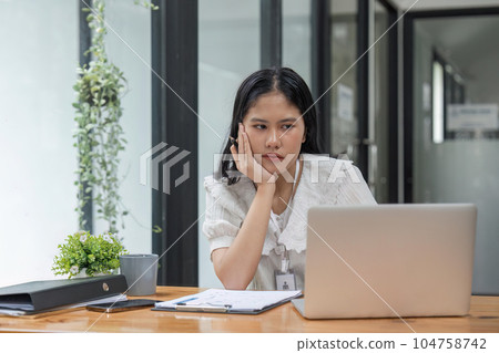Beautiful Business woman sit in front of her laptop with the stressful face and headache from her works.She sits in modern office analyzing Beautiful Business woman sit in front of her laptop with the stressful face and headache from her works.She sits in modern office analyzing 104758742
