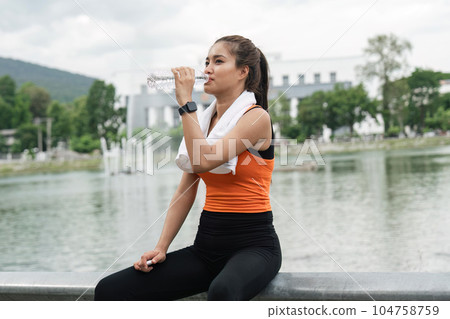 Young asian woman drinking water from bottle during workout in park 104758759
