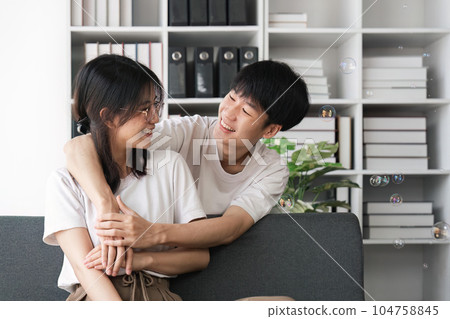 Smiling young couple embracing at office. Smiling man embracing from behind her happy girlfriend 104758845
