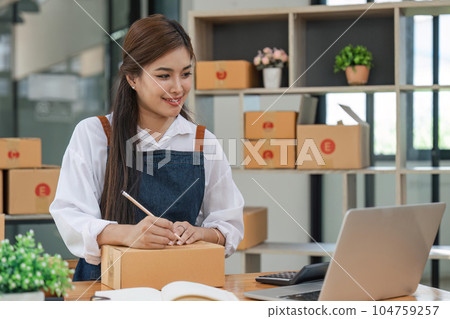 Woman who e-commerce business is writing a list of customers on paper before shipping to them, she runs an e-commerce business on websites and social media. Concept of selling products online 104759257