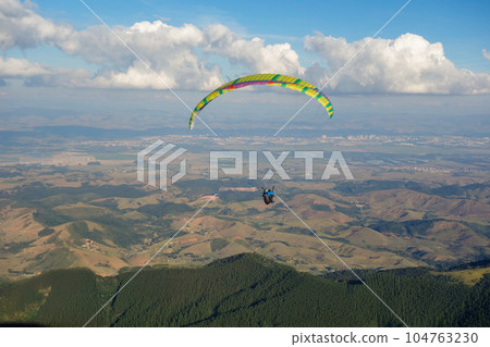 colored Paraglider flying over mountain valley on a sunny clear day 104763230