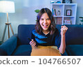 Asian woman watching TV and cheering sport games competition with laugh victory on sofa at home. 104766507