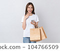 Asian woman holding brown blank craft paper shopping bags and using smartphone on white background. 104766509