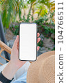 Woman sitting on the chair near swimming pool with hand holding smartphone mockup of blank screen. 104766511