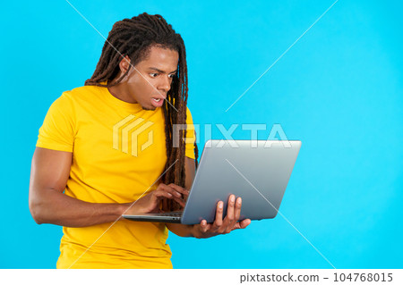 Surprised latin man with dreadlocks using a laptop Surprised latin man with dreadlocks using a laptop 104768015