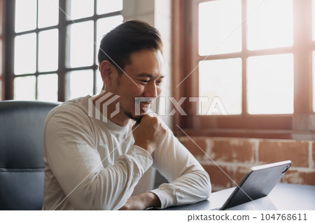 Happy man doing work online from his tablet in his own office. 104768611