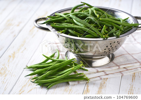 fresh green beans in a stainless steel colander on a white wooden table, selective focus. 104769600
