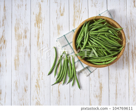 fresh green beans in a bowl on a white wooden table, top view. 104769611