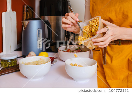Female hands putting steamed chickpeas into a bowl 104772351