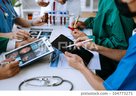Medical team having a meeting with doctors in white lab coats and surgical scrubs seated at a table discussing a patients working online using computers Medical team having a meeting with doctors in white lab coats and surgical scrubs seated at a table discussing a patients working online using computers 104773271