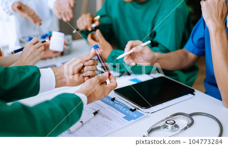 Medical team having a meeting with doctors in white lab coats and surgical scrubs seated at a table discussing a patients working online using computers 104773284