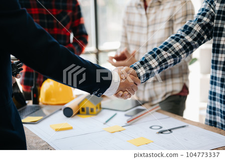 Construction team shake hands greeting start new project plan behind yellow helmet on desk in office center to consults about their building project.. Construction team shake hands greeting start new project plan behind yellow helmet on desk in office center to consults about their building project.. 104773337