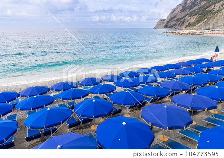 Colorful umbrellas and chairs along the beach front of Monterosso coast, one of the village in Cinque Terre, Italy 104773595