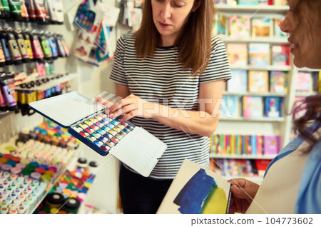 Selective focus. Female seller holding a metal case with watercolor paints in removable refills. School stationery store 104773602