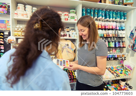 Smiling woman, seller in art shop, showing colorful vibrant watercolors in a palette with refills to a female customer 104773603