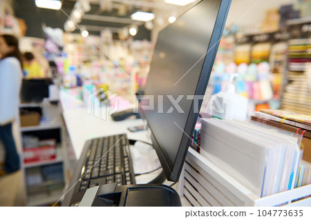 Partial view of a currency counter, note counting machine and PC monitor on the reception desk in school stationery shop 104773635
