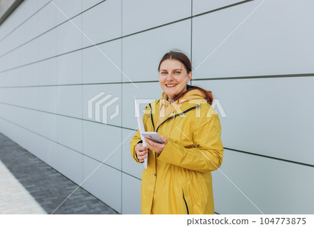 Young woman in yellow uniform using smartphone and holding package. Delivery service holding to sent a white package letter, for mockup 104773875