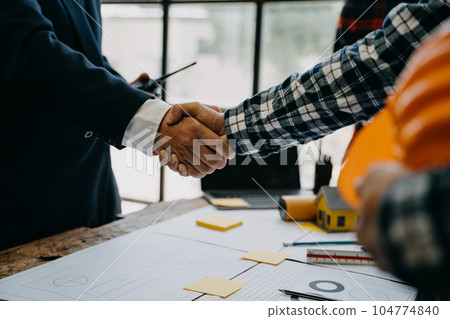 Construction workers, architects and engineers shake hands while working for teamwork and cooperation after completing an agreement in an office facility, successful cooperation concept. Construction workers, architects and engineers shake hands while working for teamwork and cooperation after completing an agreement in an office facility, successful cooperation concept. 104774840