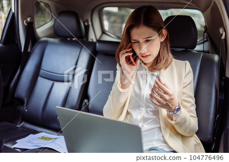 Businesswoman talking on the mobile phone and using the laptop in the car. 104776496