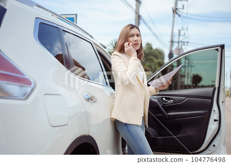 Unhappy businesswoman standing near car holding documentand using mobile phone. 104776498