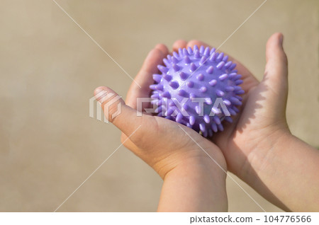 Close-up of a child's hands holding a purple prickly antistress ball. Close-up of a child's hands holding a purple prickly antistress ball. 104776566