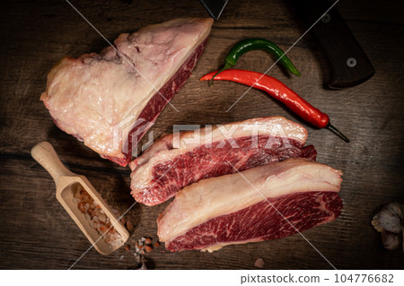 Organic machete or hanger butcher steak, near butcher knife with pink pepper and rosemary. Black background. Top view. side view Organic machete or hanger butcher steak, near butcher knife with pink pepper and rosemary. Black background. Top view. side view 104776682