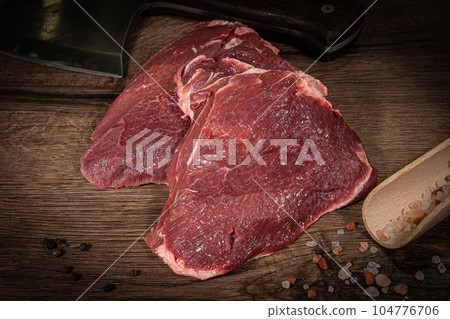 Raw hanging tender or onglet steak of beef on wooden Board with rosemary and thyme on wooden background 104776706