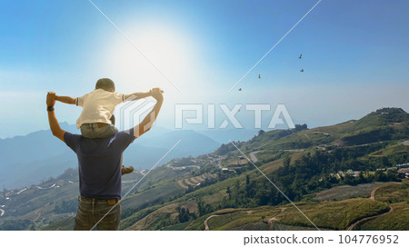 Father and son over meadowputs his son on his shoulder. The family life journey concept Father and son over meadowputs his son on his shoulder. The family life journey concept 104776952