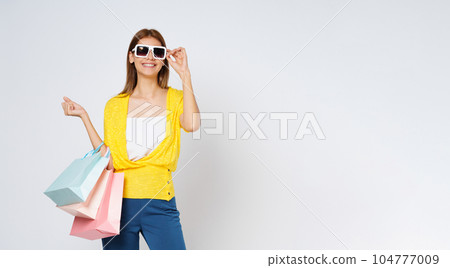 Happy young woman wearing sunglasses and holding  shopping bags isolated on white background. 104777009