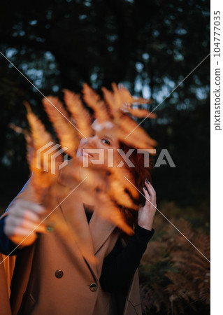 Young woman hiding behind fern leaf in dark forest 104777035