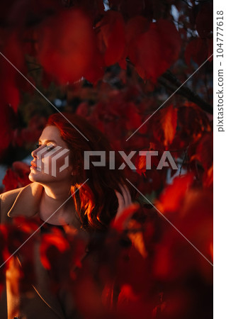 Portrait red-haired woman with closed eyes standing in red autumn trees Portrait red-haired woman with closed eyes standing in red autumn trees 104777618