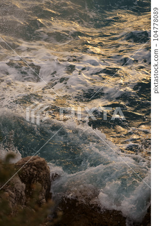 Sea waves crashing against the rocks of mediterranean shore during sunset Sea waves crashing against the rocks of mediterranean shore during sunset 104778089