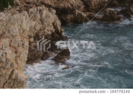 Sea waves crashing against the rocks of mediterranean shore Sea waves crashing against the rocks of mediterranean shore 104778148