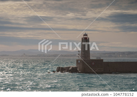Nice port lighthouse in the harbor at sunset with uncalm sea Nice port lighthouse in the harbor at sunset with uncalm sea 104778152