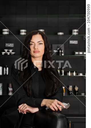 Beautiful young brutal woman male master hairdresser, barber holding razor for shaving on the background of a wall with beard and hair care 104780999