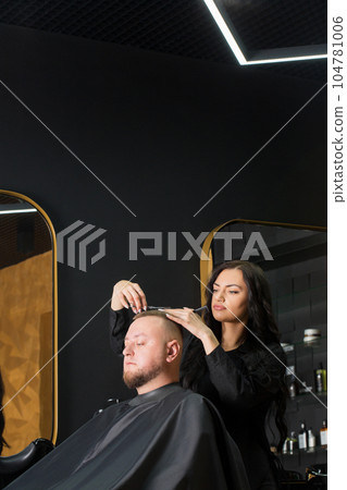 woman male master hairdresser makes a man's hair with scissors in a barbershop 104781006