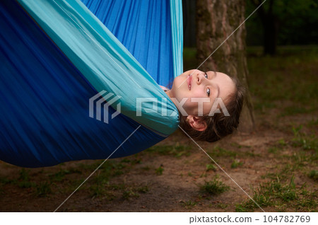 Close-up adorable little child girl lying on a blue hammock in a summer camp, smiling looking at camera. Happy childhood 104782769