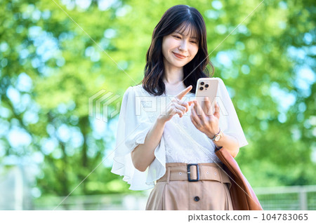 Business woman operating a smartphone in front of fresh green Business woman operating a smartphone in front of fresh green 104783065