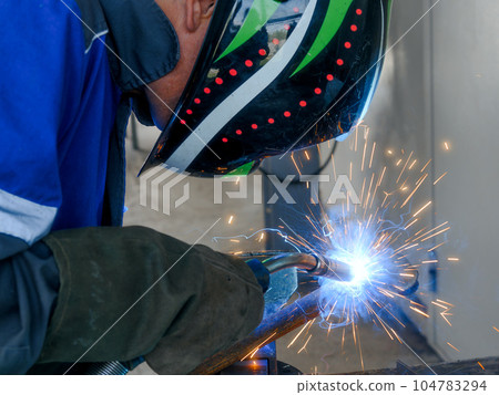 The welder works at the factory in the production workshop. a masked gas welder welds a metal pipe The welder works at the factory in the production workshop. a masked gas welder welds a metal pipe 104783294