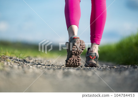 Low angle view of hiking shoe sole while walking on gravel trail 104784453