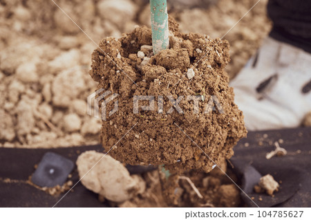 A man drills a hole with a hand drill through agro fiber, field and manual work. 104785627