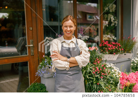 Smiling woman florist small business owner standing with crossed arms near own floral store Smiling woman florist small business owner standing with crossed arms near own floral store 104785658