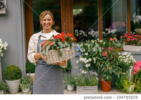 Smiling woman florist business owner standing with houseplant on background of floral store Smiling woman florist business owner standing with houseplant on background of floral store 104785659