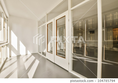 an empty room with large windows and sun shining through the window panes on the right side of the room 104785794