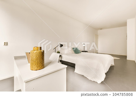 a bedroom with a bed, nightstand and lamp on the side of the bed there is a large yellow vase next to the bed 104785808