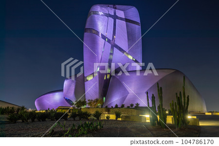 Illuminated during the night modern building in the center of Al Khobar with green cactuses in the foreground, Saudi Arabia 104786170
